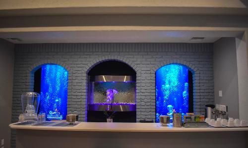A home bar with three arched, glowing blue aquariums built into a grey brick wall.