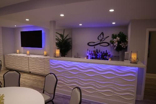 A home bar area featuring white, wavy textured cabinets, purple under-counter lighting, a TV, and decorative candles.