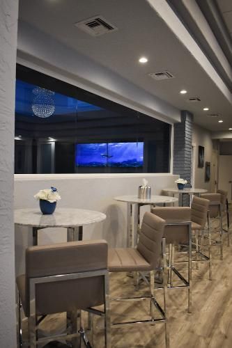 A modern indoor seating area with high-top tables, gray leather bar stools, and a large window overlooking a night scene.