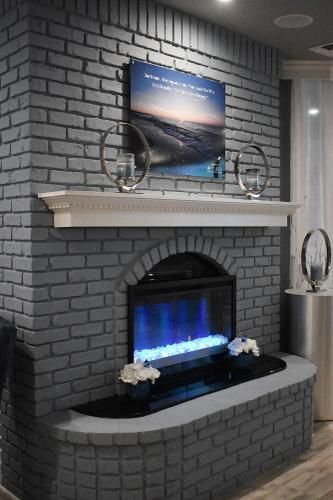 An arched electric fireplace set in a gray brick wall with a white mantle, decorative metal hoops, and floral accents.