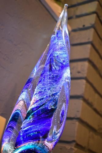 A close-up of a decorative, flame-shaped glass sculpture with swirling blue, purple, and iridescent patterns.