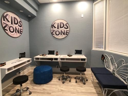 A blue-walled Kids Zone room with white workstations, a blue ottoman, wheeled stools, and a butterfly-style bench.