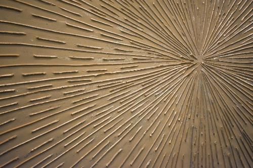 Abstract textured gold surface with radiating lines creating a sunburst effect from a central point.