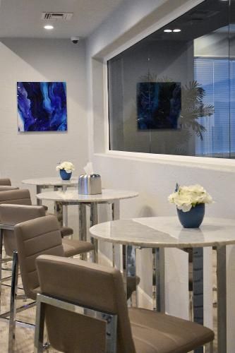 Two marble-topped tables with flower vases in a modern office lounge, with blue abstract wall art.
