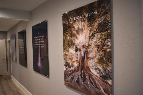 A hallway with four framed inspirational posters displayed on a gray wall, focusing on one depicting a large tree.