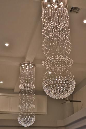 Two cascading crystal chandeliers hanging from a neutral-colored ceiling in a room.