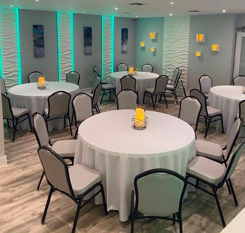 A banquet room with round tables, grey chairs, and walls featuring textured vertical panels lit by green and yellow lights.