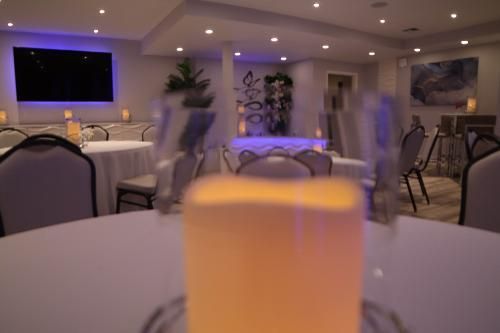 A candle on a white table in a dimly lit event space with circular tables, chairs, and ambient blue and warm lighting.