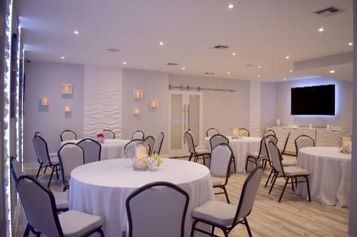 A well-lit, modern event room with round tables covered in white tablecloths and light grey chairs, with wall lighting.