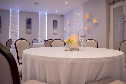 A dining room set with white-clothed round tables, upholstered chairs, and decorative wall lighting with wave textures.