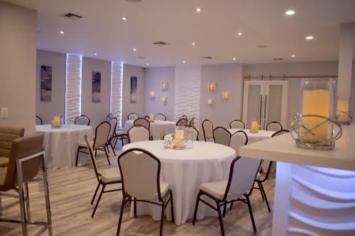 A modern event space featuring white-clothed round tables, matching chairs, and ambient wall lighting in soft neutral tones.