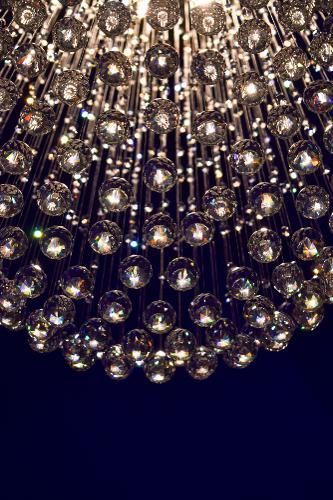 A close-up view of a tiered chandelier featuring numerous spherical, faceted glass beads illuminated against a dark background.