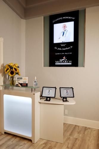 A reception desk with sunflowers and two tablets below a wall sign honoring Dr. John Robinson Sr. at Monarch.