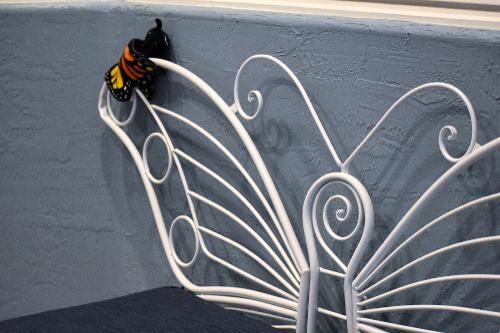 A decorative white wrought-iron butterfly headboard stands against a grey wall with a small fabric butterfly attached.