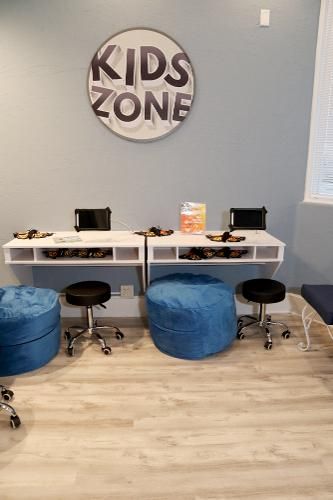 A kids' zone area with two white wall-mounted desks, black rolling stools, and blue beanbag chairs under a wall sign.