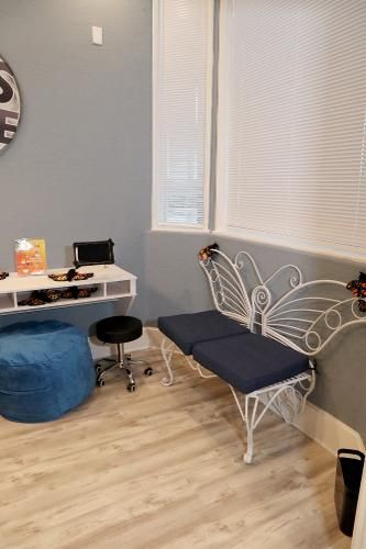 A small room with a white butterfly-shaped bench, a white desk, a rolling stool, and a large blue floor pouf on wood floors.