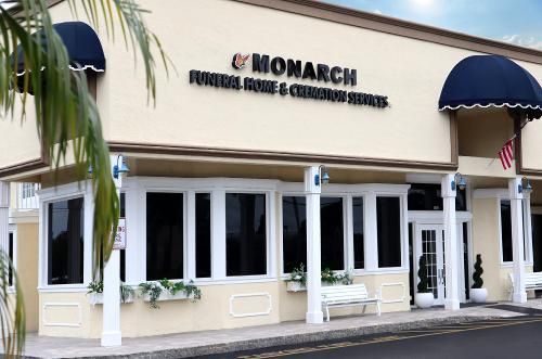 A beige Monarch Funeral Home & Cremation Services building with dark blue awnings and white columns.