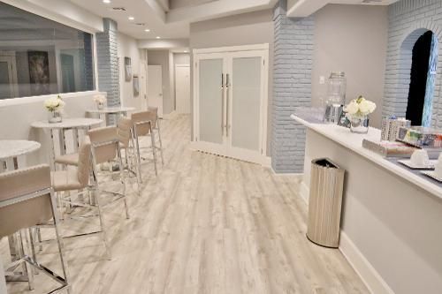 Modern, light-toned lounge or reception area with high-top tables, chairs, a long serving counter, and French doors.