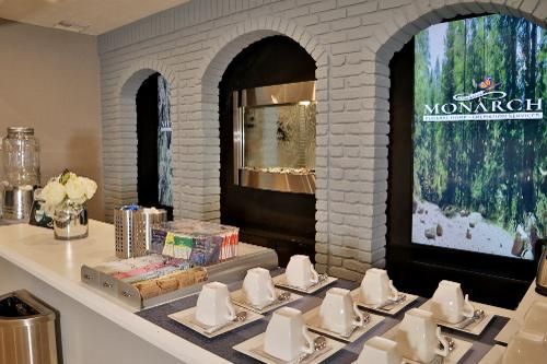 A refreshment station with white coffee mugs, sugar packets, and a water dispenser in front of a white brick wall.