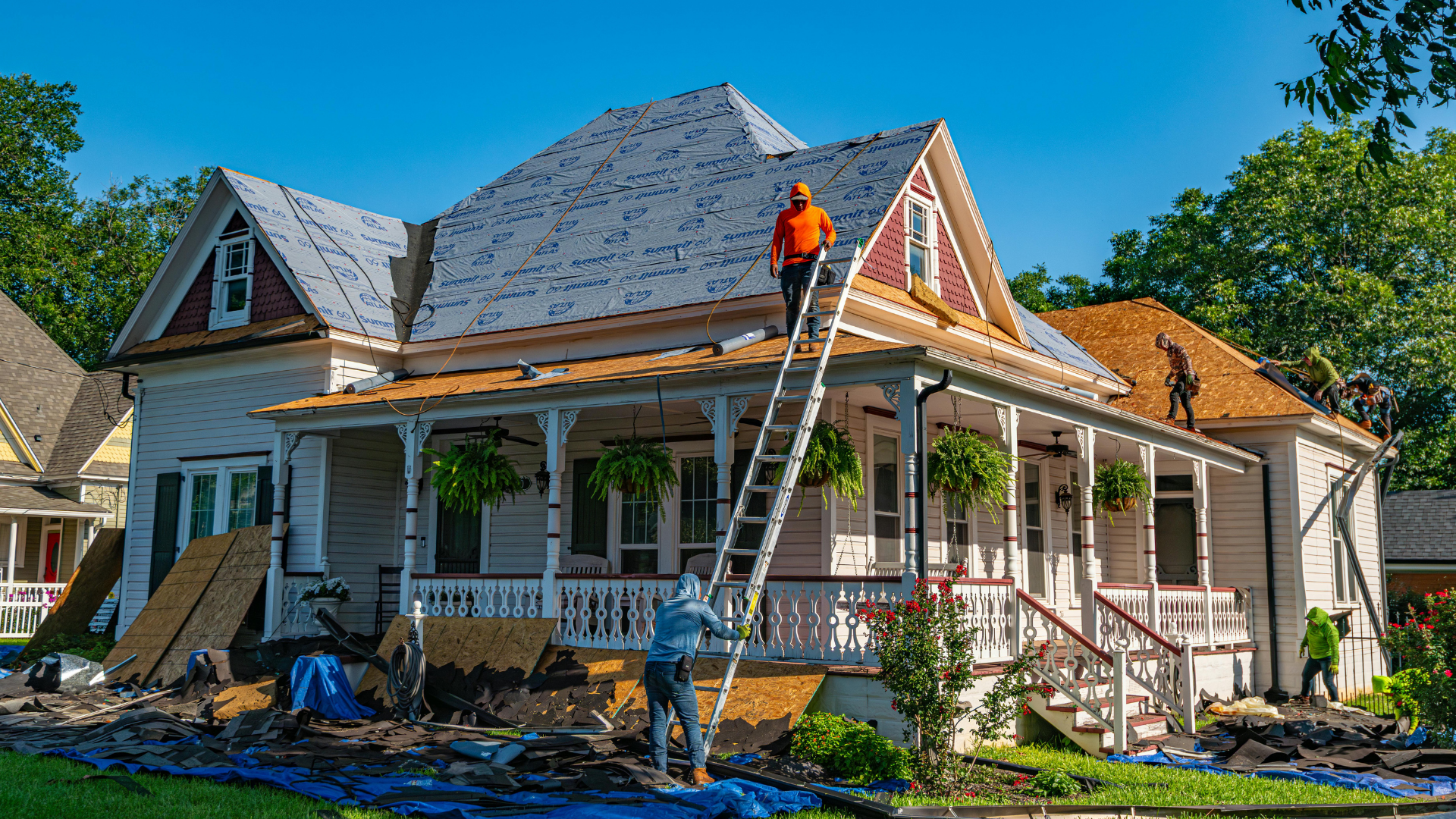 Two workers on ladders repairing a house roof and porch in bright daylight