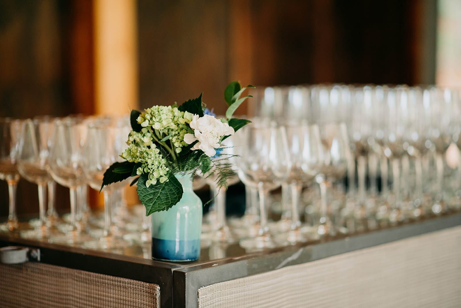 A vase of flowers is sitting on a table next to a row of wine glasses.