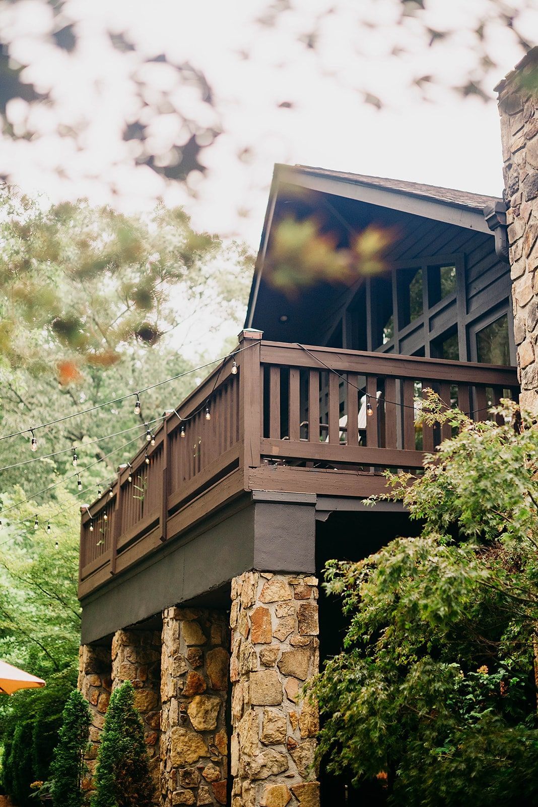 A large wooden deck on the side of a house surrounded by trees.