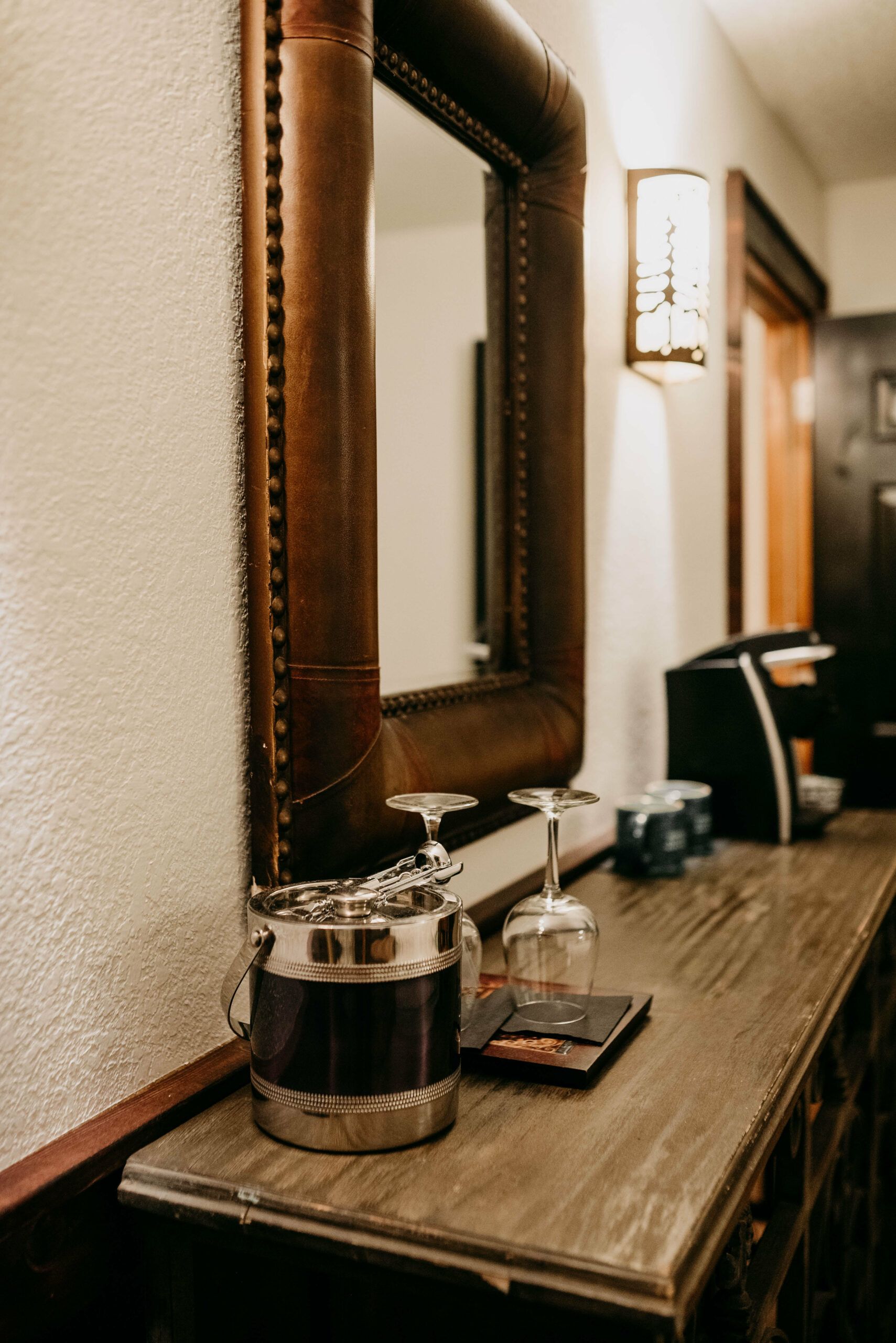 A wooden table with a mirror and wine glasses on it.