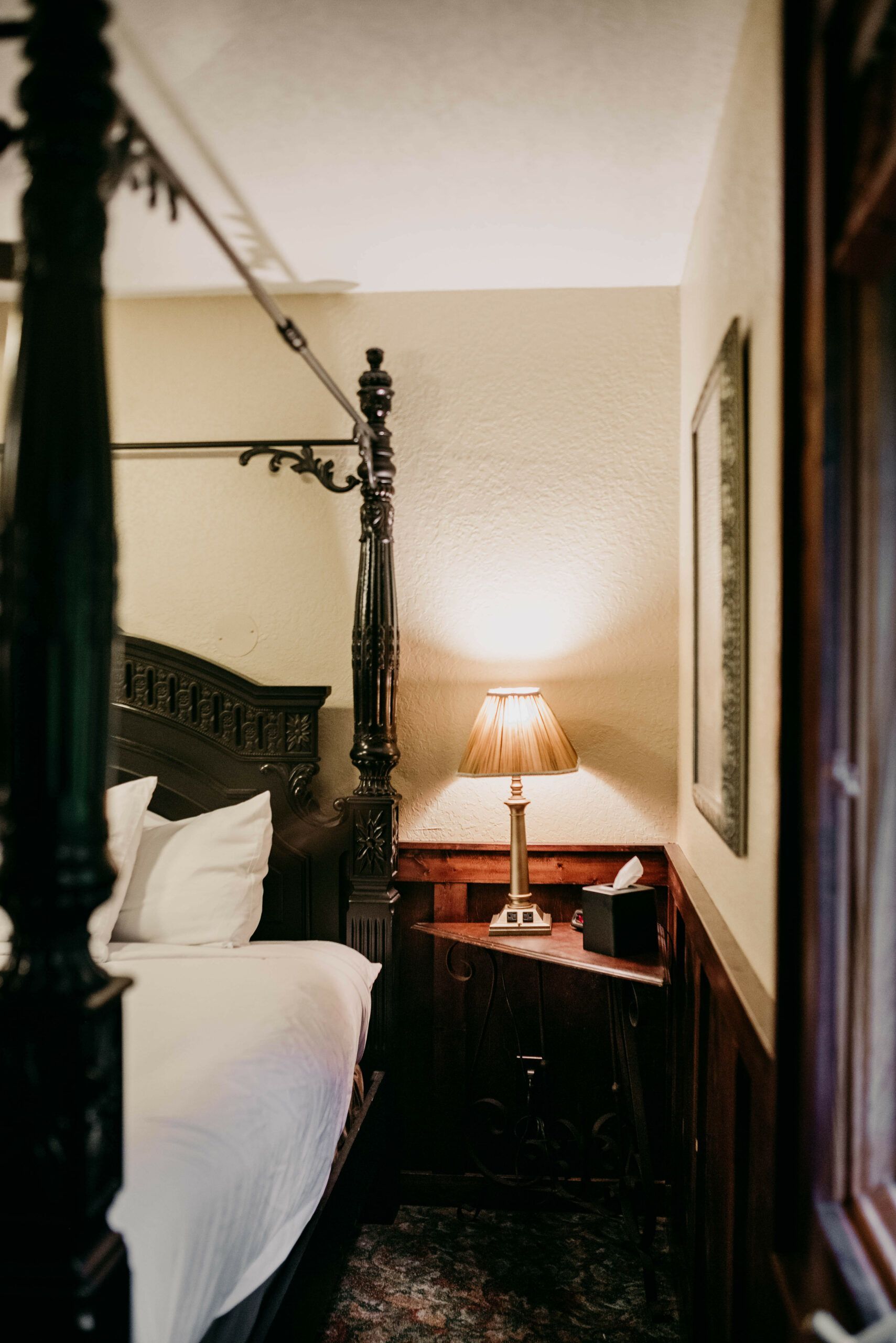A bedroom with a canopy bed , nightstand , lamp and window.
