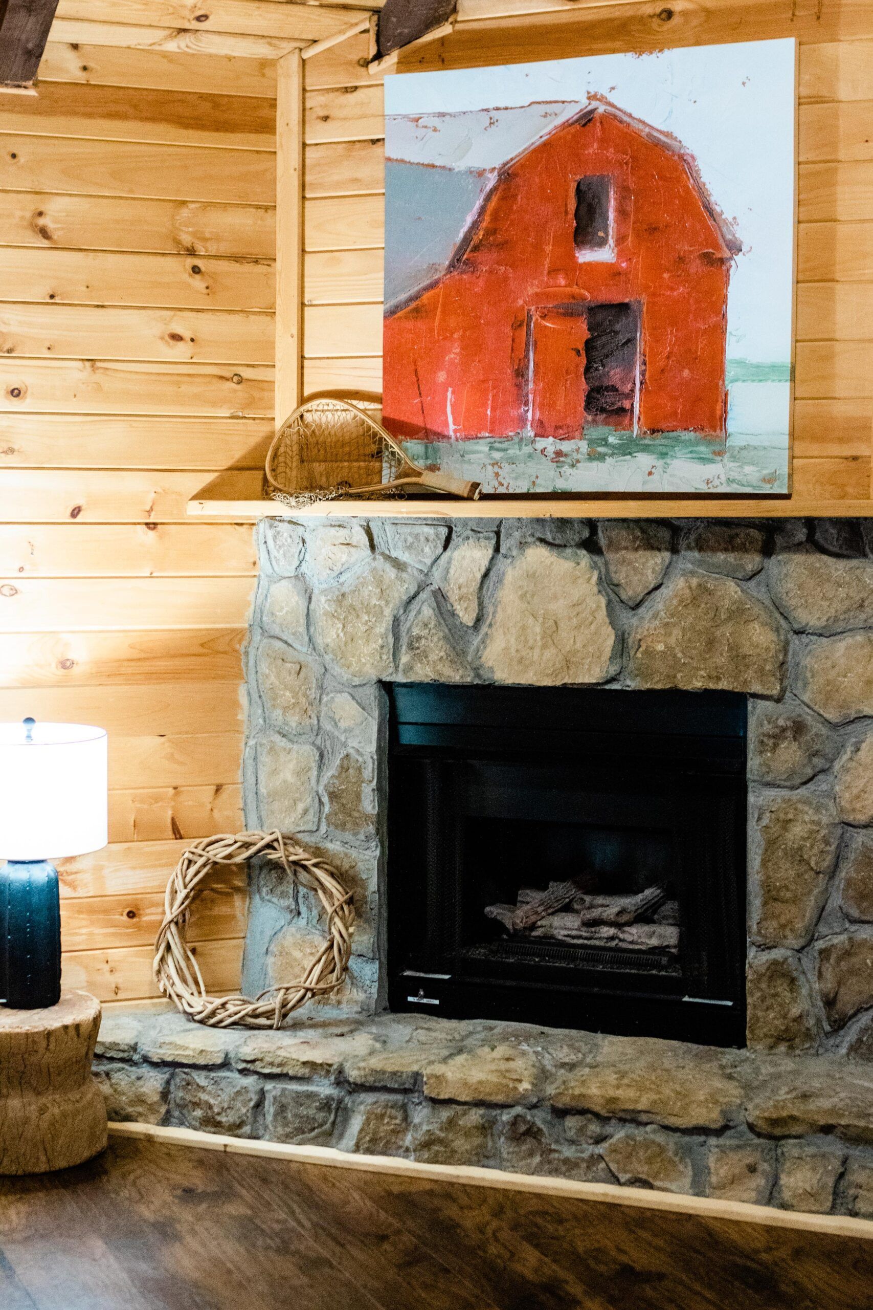 A living room with a fireplace and a painting of a barn on the wall.