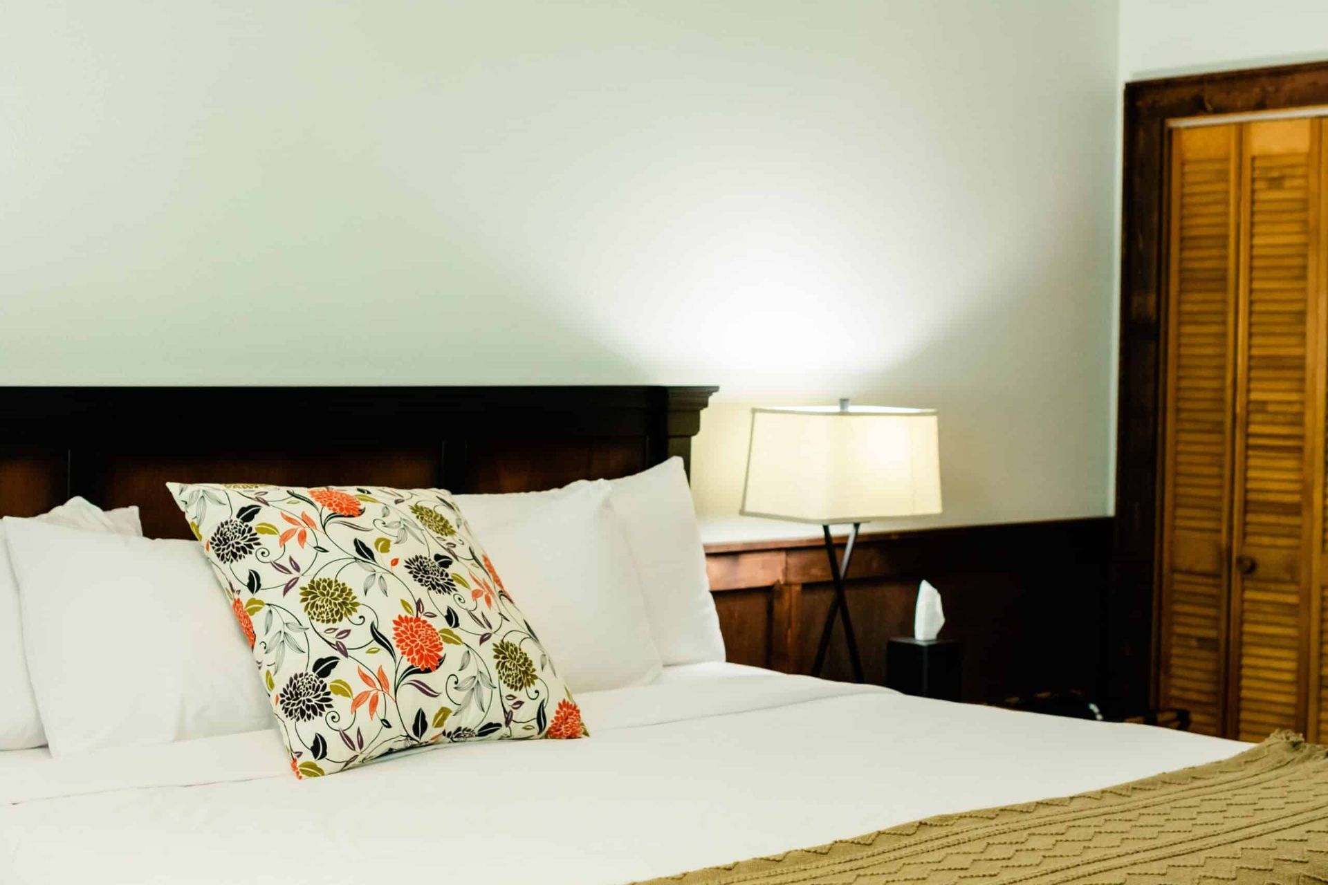 A bed with white sheets and a floral pillow in a hotel room.
