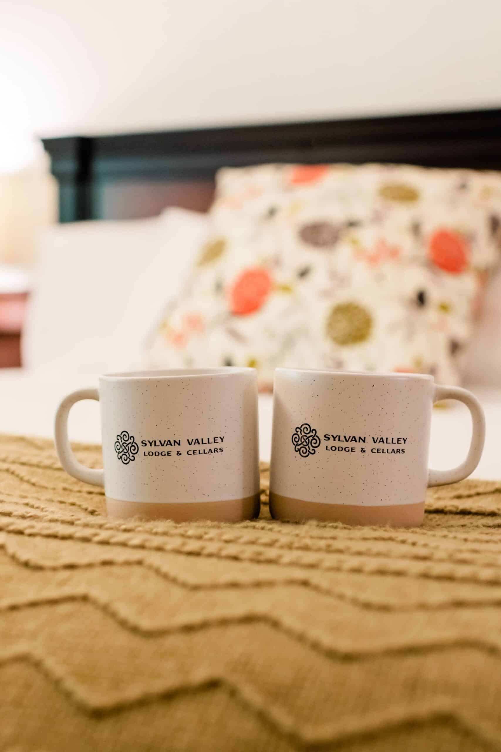 Two coffee mugs are sitting on top of a bed.