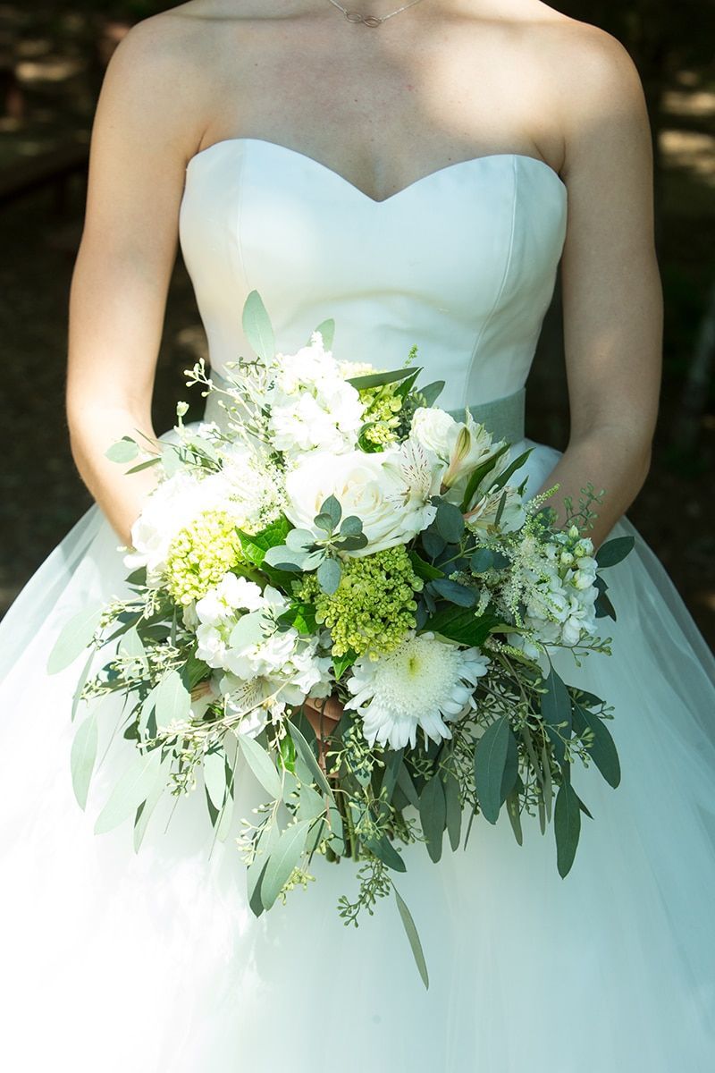 A bride in a white dress is holding a bouquet of white flowers.