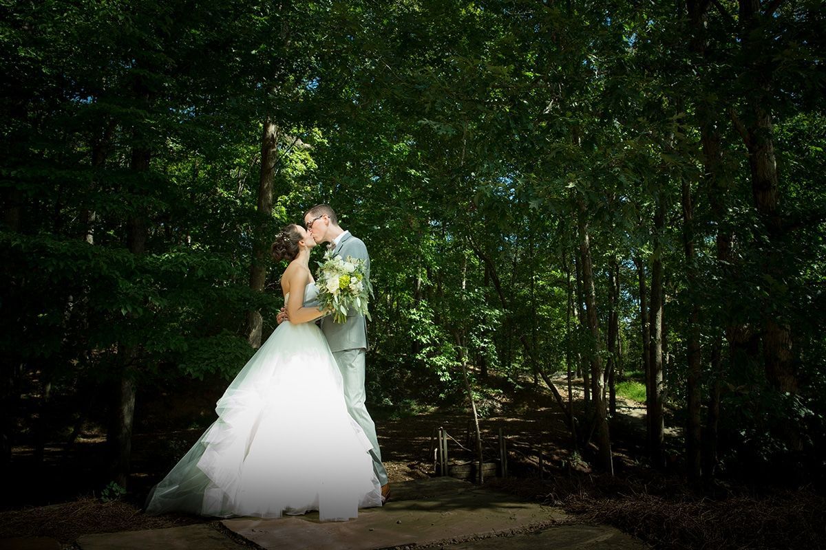 A bride and groom are kissing in the woods.