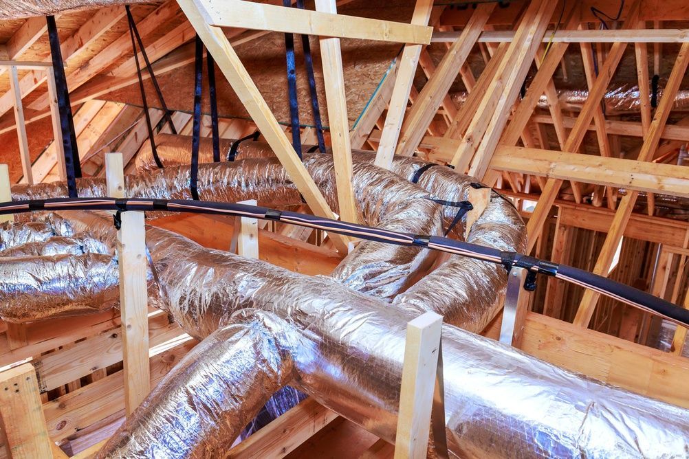 Attic framing with exposed wooden trusses and large silver insulated HVAC ducts