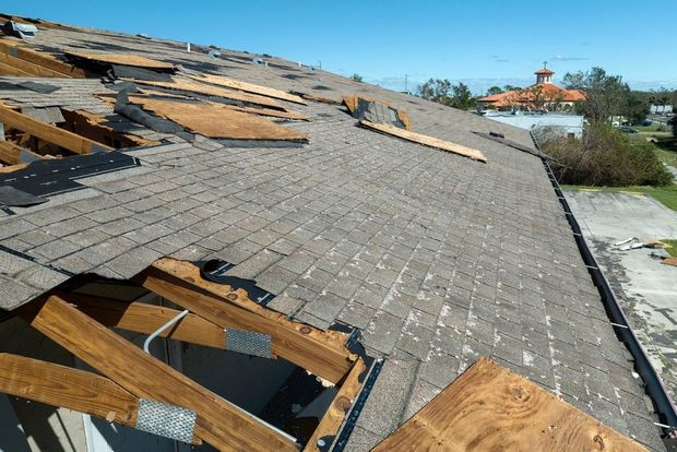 Damaged roof with missing shingles and exposed wooden framing under a clear blue sky