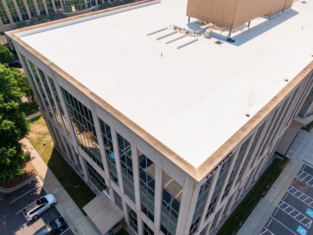 Aerial view of a modern office building with a large white roof and beige rooftop structure.