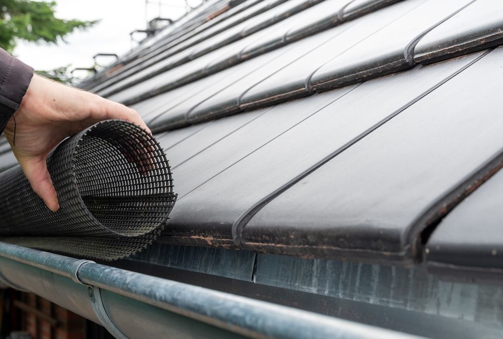 Hand placing black gutter guard mesh over a roof gutter on a metal roof