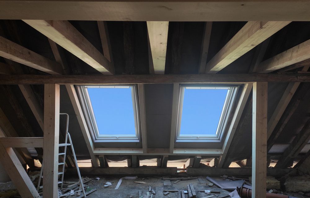 Attic interior with two skylights, exposed beams, and a ladder against the left wall.