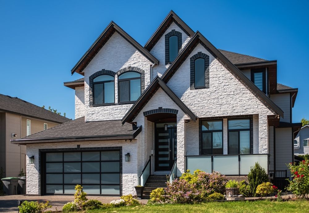 Modern two-story white house with dark trim, gabled roof, garage, and front landscaping under a blue sky
