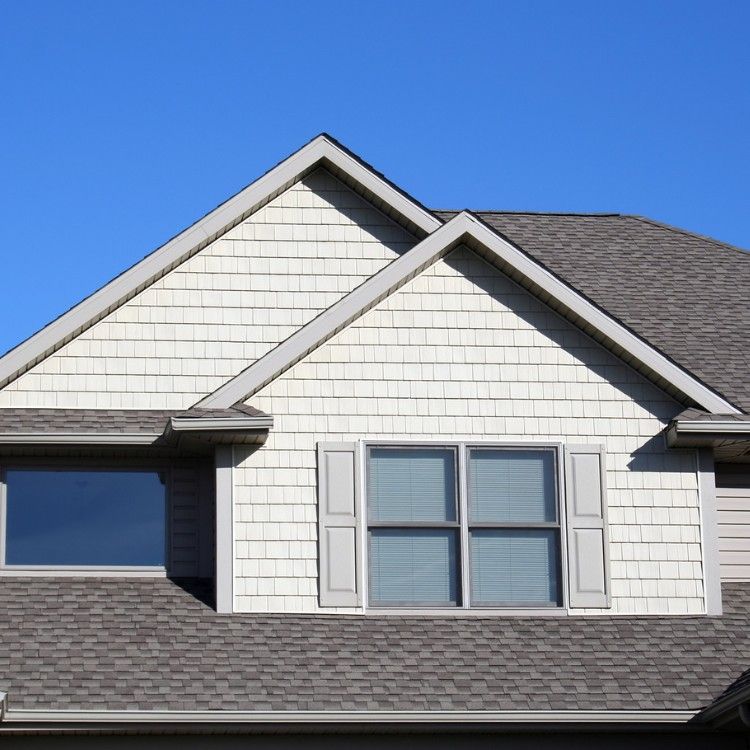 Suburban house roof and gable with white siding, gray shingles, and blue sky