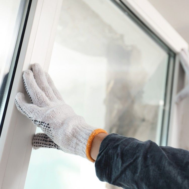 Gloved hand cleaning a white window frame with a cloth