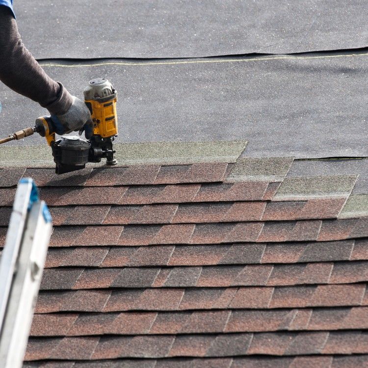 Roofing worker using a nail gun on asphalt shingles during roof repair