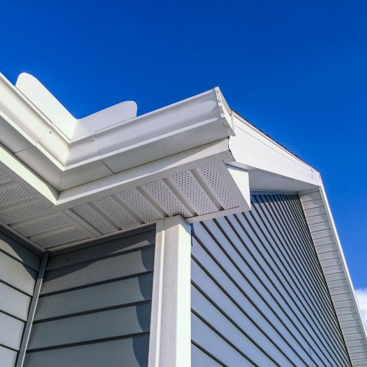 White house eaves and gray siding against a bright blue sky