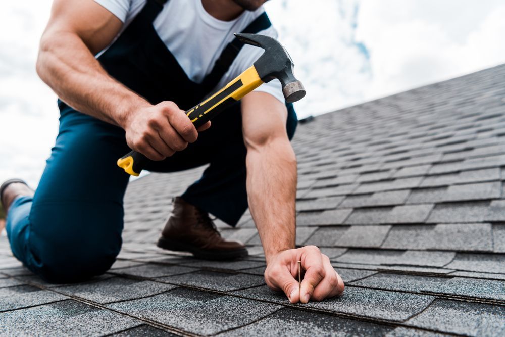 Worker inspecting roof shingles with a hammer on a sloped rooftop