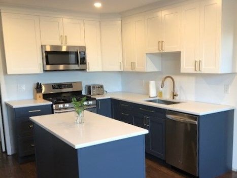 A kitchen with blue cabinets , white counter tops , stainless steel appliances and a large island.