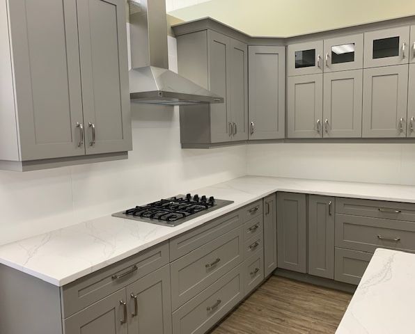 A kitchen with gray cabinets and white counter tops and a stove top oven.