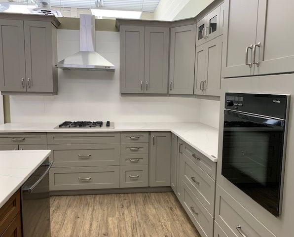 A kitchen with gray cabinets , white counter tops , stainless steel appliances and a stove.