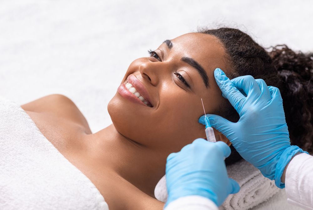 A medical professional in blue gloves administers a facial injection to a person resting on a table.