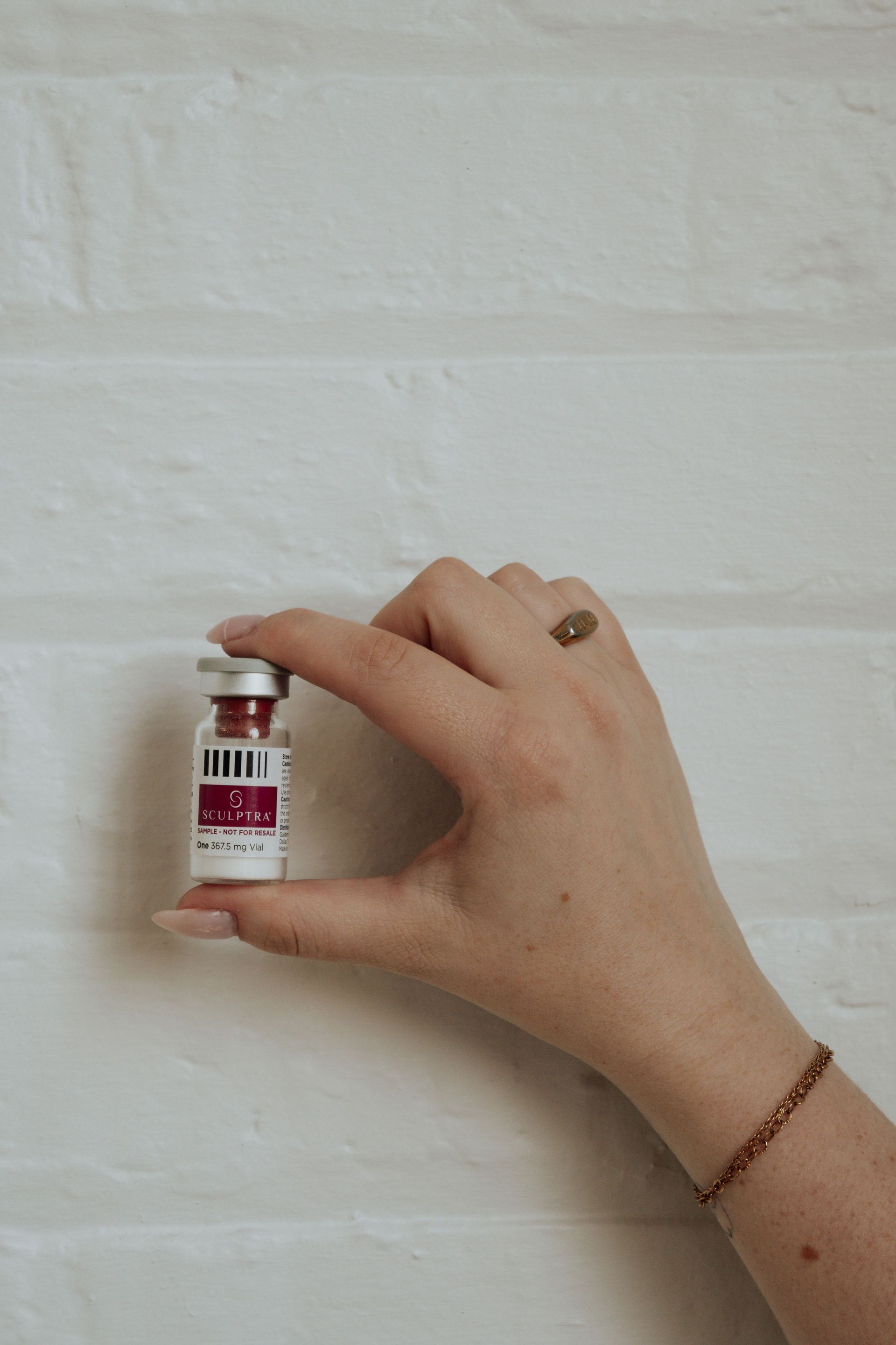 Hand holding a small vial of a red liquid against a white brick wall.