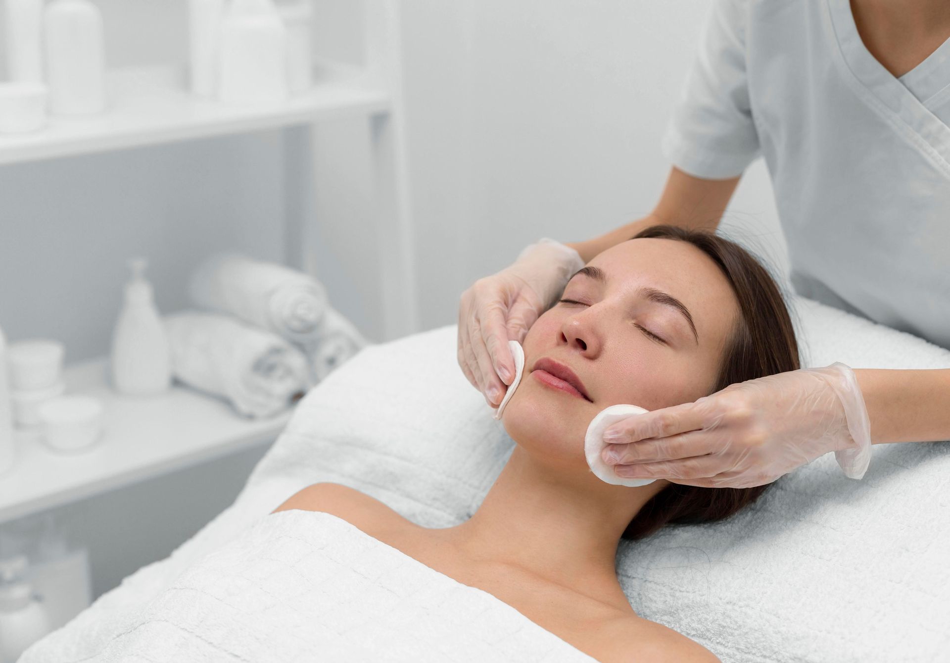 Woman receiving facial massage treatment in a spa, lying on a bed with eyes closed